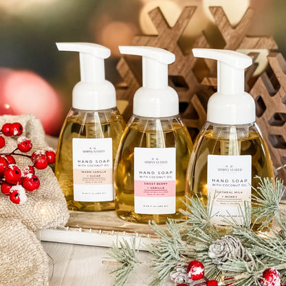 Three bottles of hand soap with pump dispensers on a decorative surface with Christmas elements.
