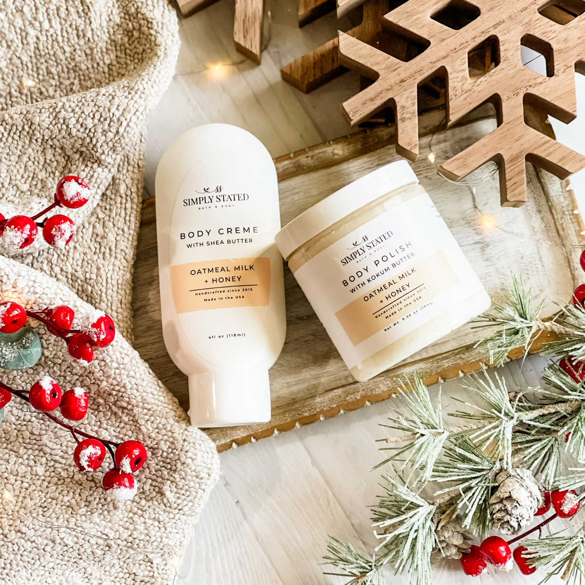 Simply Stated Oatmeal Milk + Honey Body Creme and Body Polish duo, styled with wooden snowflake, berries, and frosted pine.