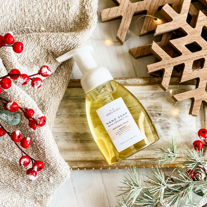 Simply Stated oatmeal milk honey foaming hand soap with coconut oil beside holiday berries and wooden snowflakes