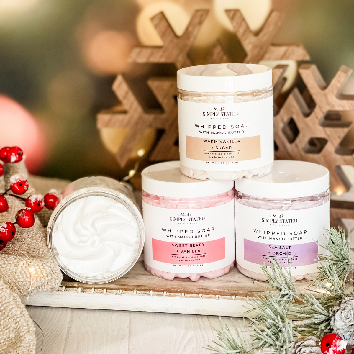 Simply Stated whipped soap with mango butter in three scents, stacked with an open jar beside holiday berries
