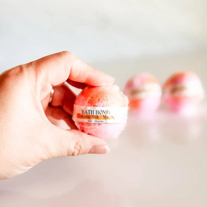 Bath Bomb in Coconut Milk + Mango, pink and orange bath bomb held in hand with more bombs blurred in background