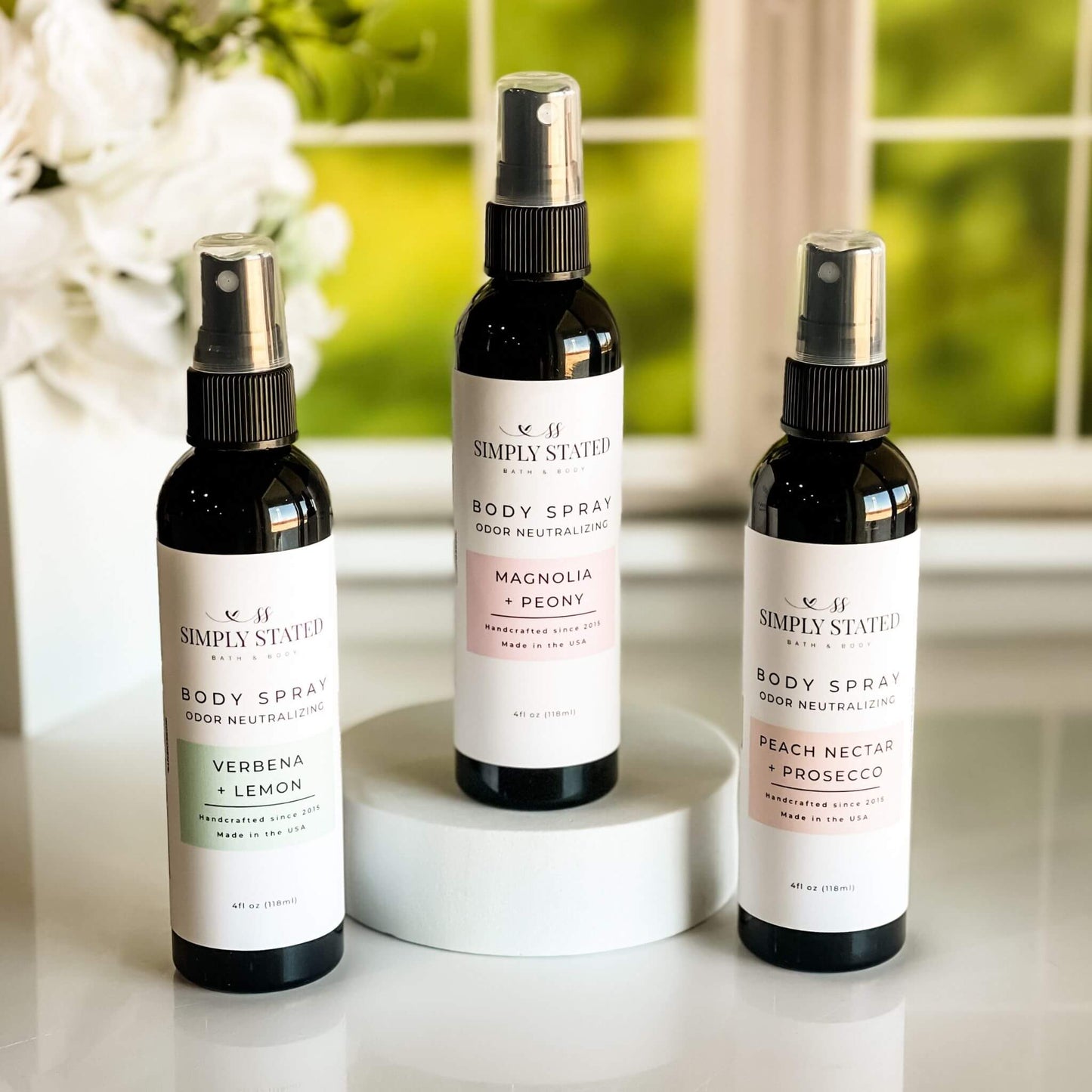 Spring Floral Orchard Collection Body Spray trio displayed with Magnolia + Peony, Peach Nectar + Prosecco, and Verbena + Lemon variants in a lush spring background.