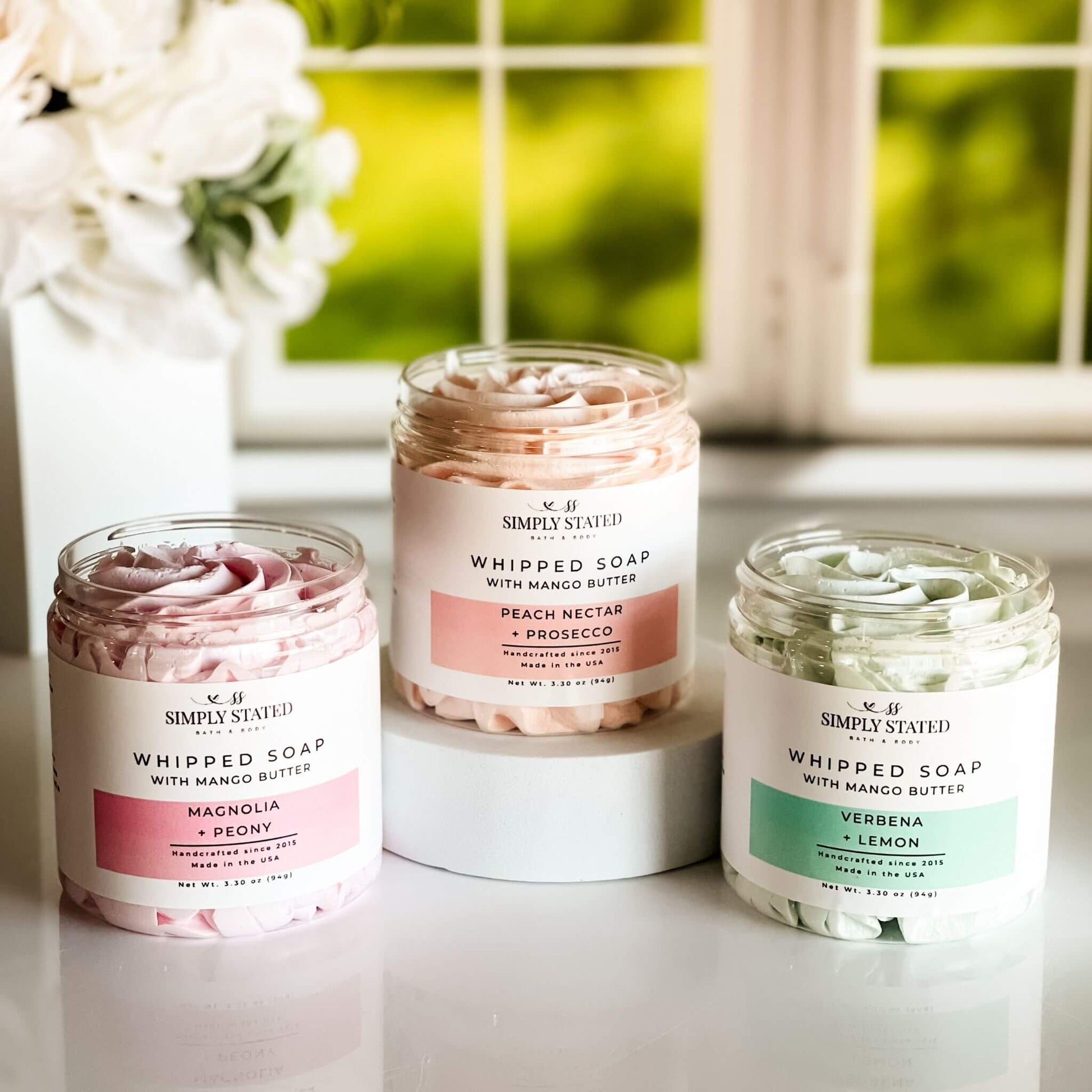 Group of three Simply Stated Spring Whipped Soap jars in seasonal scents with vibrant lush backgrounds.