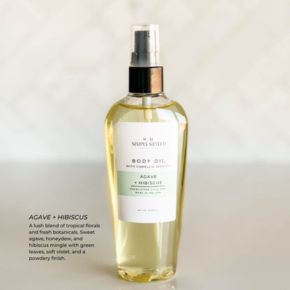 Simply Stated Bath & Body Agave + Hibiscus Body Oil bottle with camellia seed oil, photographed on a neutral backdrop. Features a soothing green label with tropical floral scent notes including sweet agave, honeydew, hibiscus, green leaves, and violet.