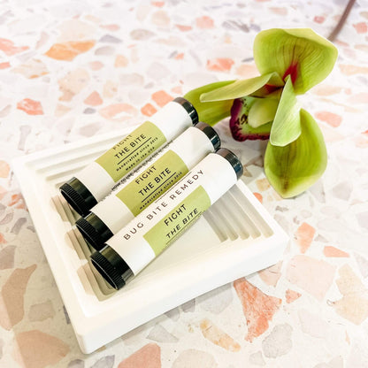 Flatlay of Fight the Bite Bug Bite Remedy Sticks with tropical flower on terrazzo background, essential oil-based summer skin care.