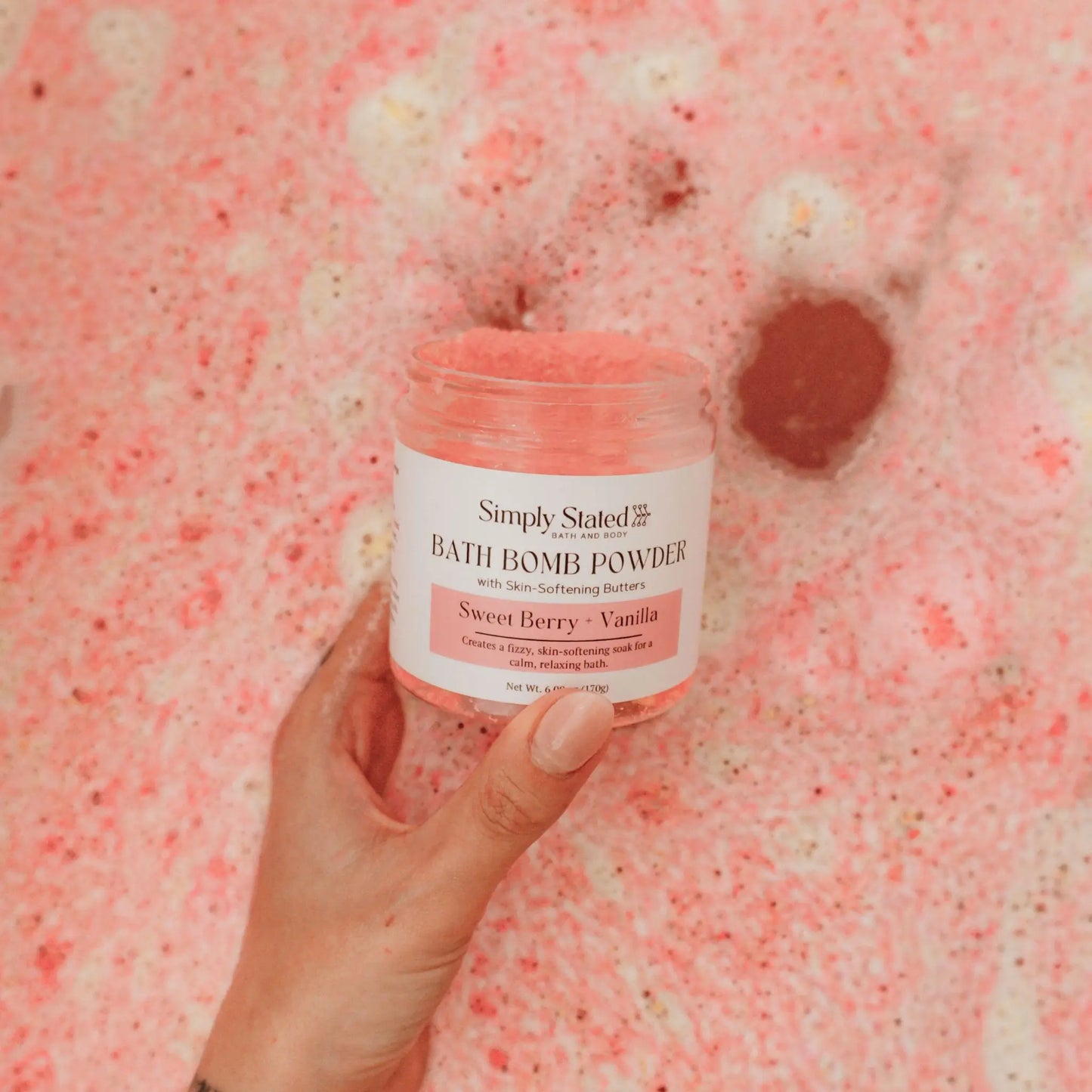 Sweet Berry + Vanilla Bath Bomb Powder jar held over pink bubble bath water