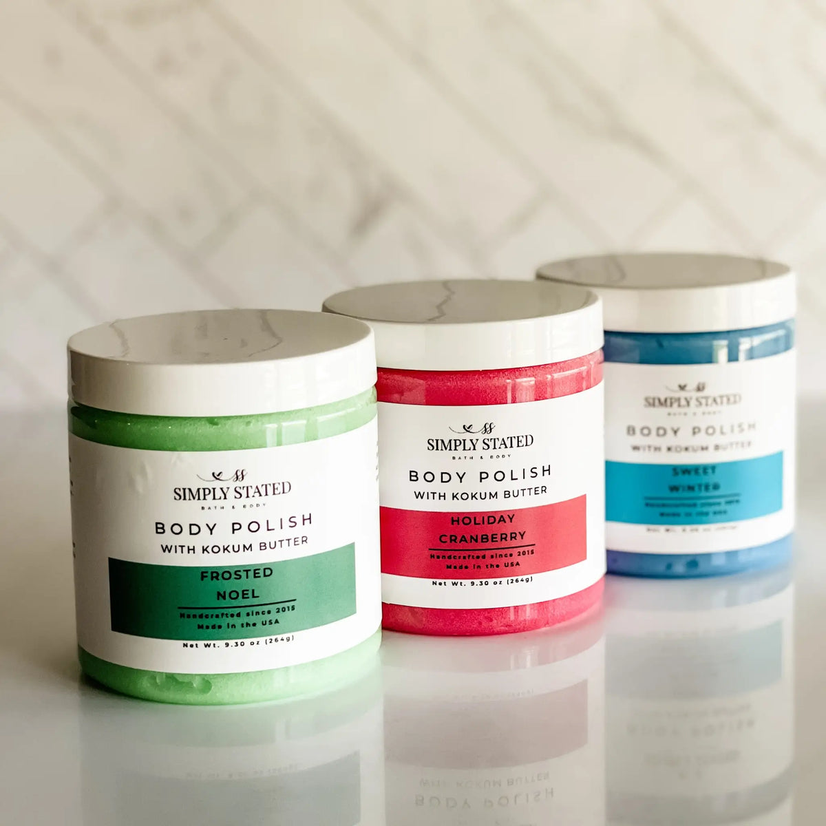 Simply Stated Body Polish trio with kokum butter, Frosted Noel, Holiday Cranberry, Sweet Winter scrubs on marble.