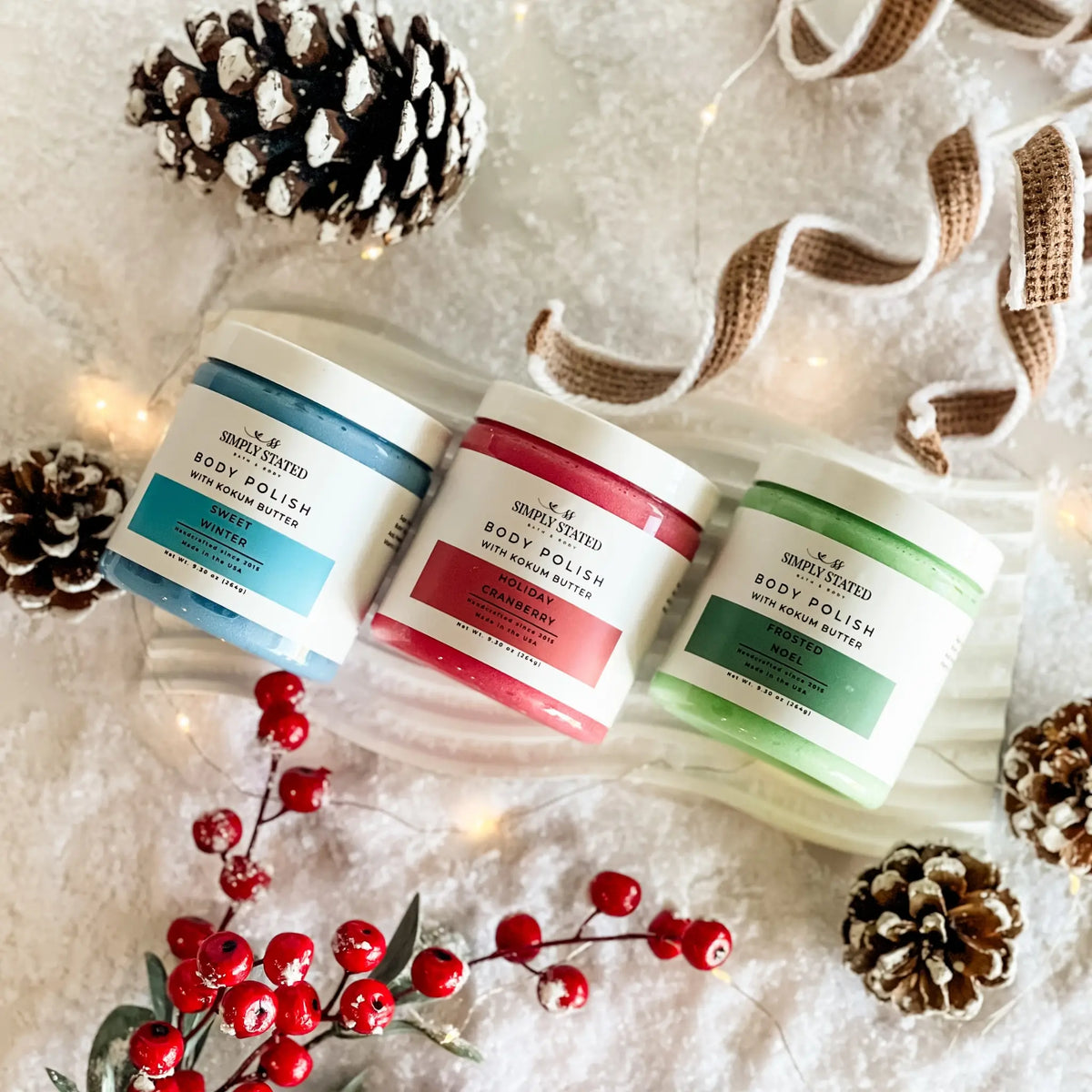 Simply Stated Body Polish trio with kokum butter, snowy holiday scene with pinecones, berries, and twinkle lights.