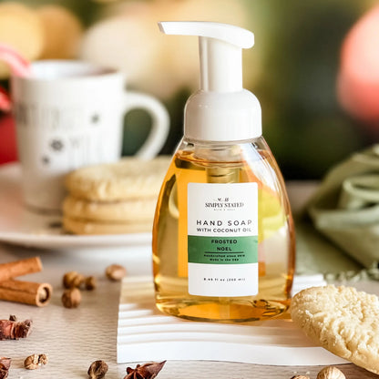 Simply Stated Frosted Noel Hand Soap with coconut oil, foaming pump bottle beside sugar cookies and cinnamon sticks.
