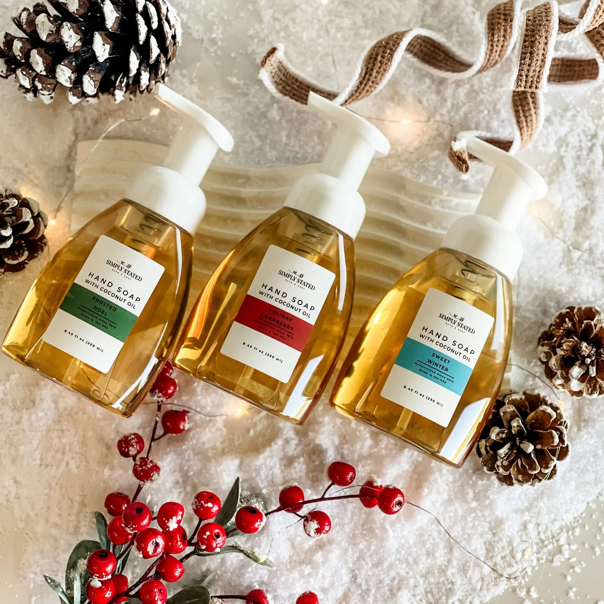 Simply Stated Foaming Hand Soap trio with coconut oil, snowy holiday scene with pinecones, red berries, and lights.