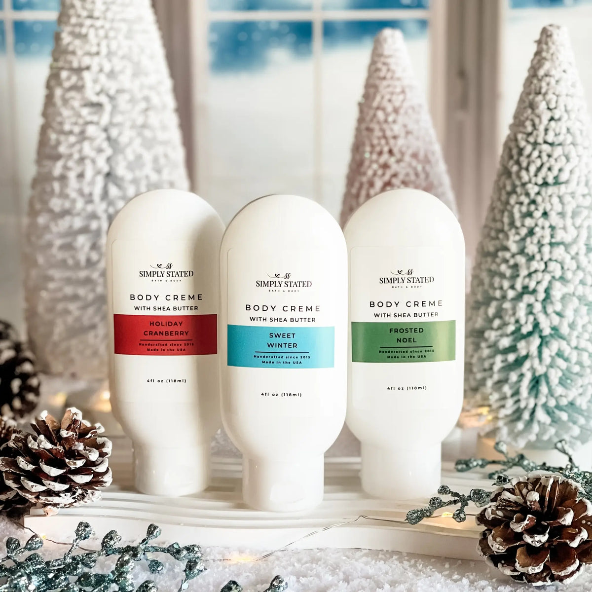 Simply Stated Body Creme trio with shea butter, Holiday Cranberry, Sweet Winter, Frosted Noel among snowy trees.