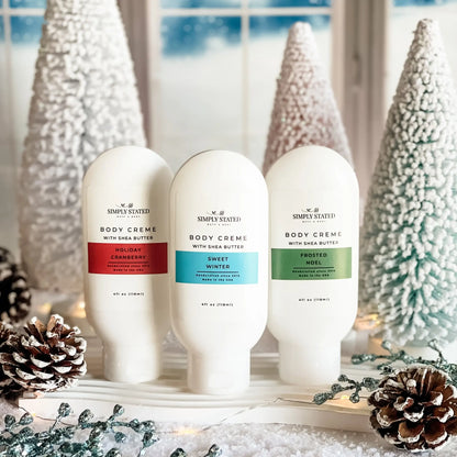Simply Stated Body Creme trio with shea butter, Holiday Cranberry, Sweet Winter, Frosted Noel among snowy trees.