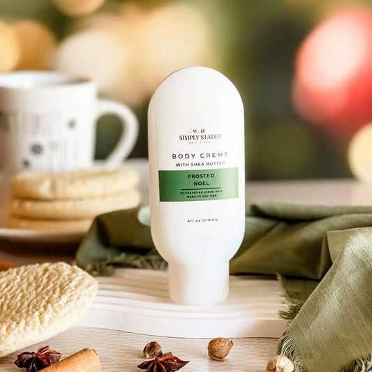 Simply Stated Frosted Noel Body Creme with shea butter, cozy holiday scene with cinnamon, star anise, and mug.
