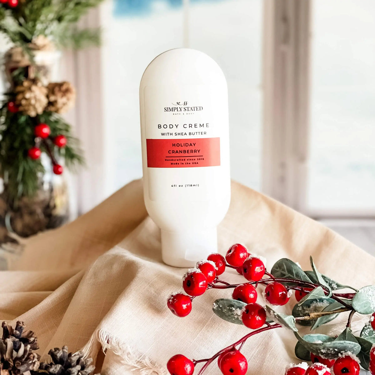 Simply Stated Holiday Cranberry Body Creme with shea butter, festive holiday scene with red berries and pinecones.