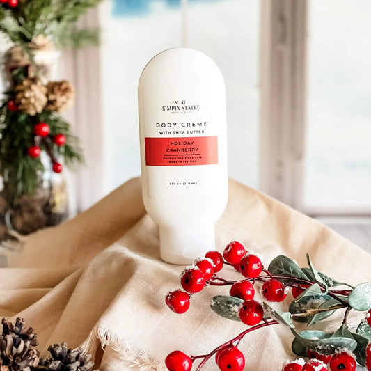 Simply Stated Holiday Cranberry Body Creme with shea butter, festive holiday scene with red berries and pinecones.