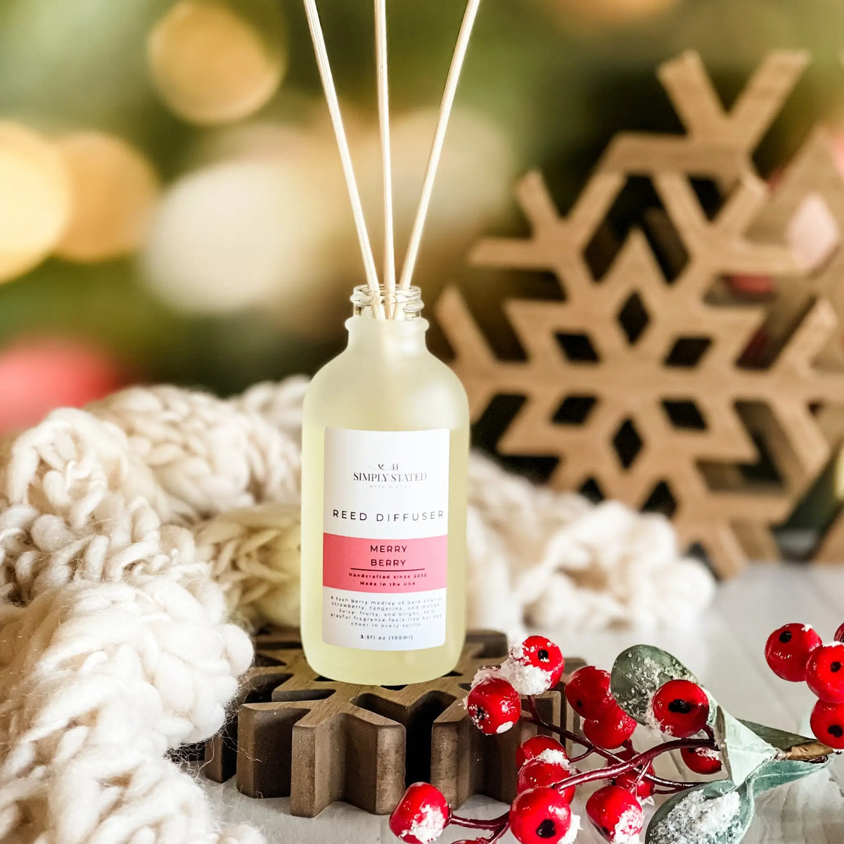 Simply Stated Merry Berry Reed Diffuser in frosted glass, styled with a wooden snowflake, cozy knit, and red berries.