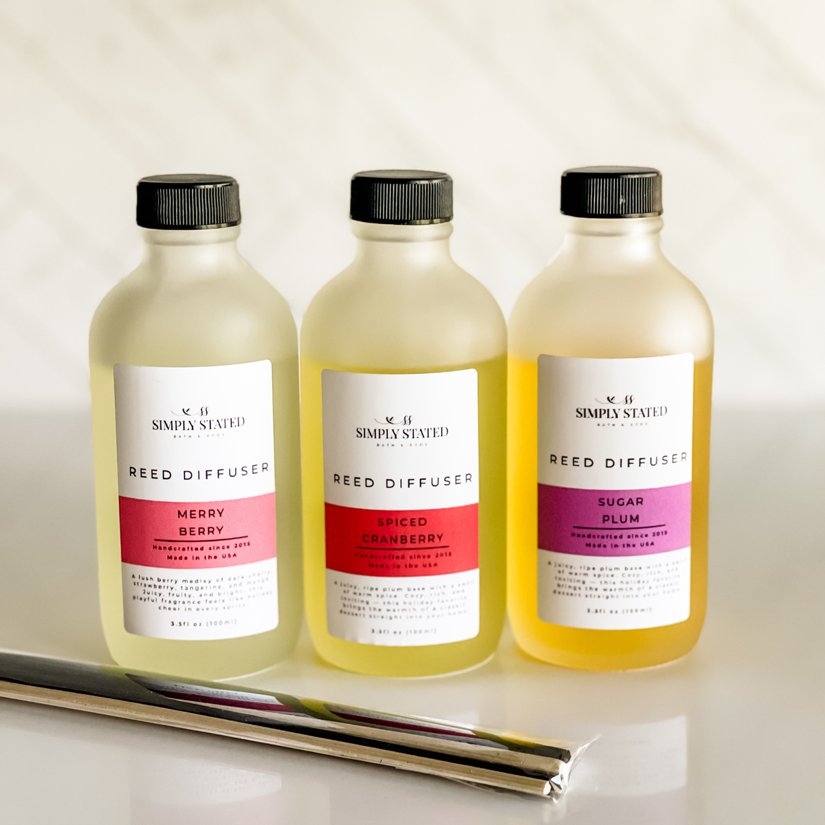 Simply Stated Reed Diffuser trio in frosted glass, Merry Berry, Spiced Cranberry, Sugar Plum, with reeds on marble.