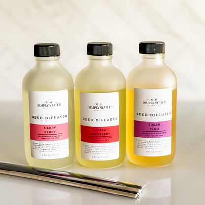Simply Stated Reed Diffuser trio in frosted glass, Merry Berry, Spiced Cranberry, Sugar Plum, with reeds on marble.