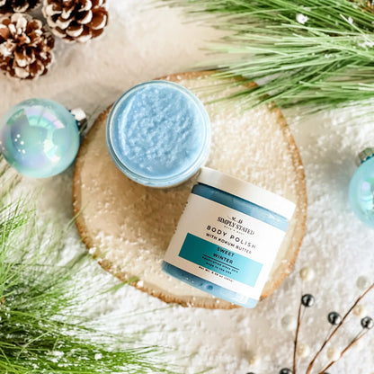 Simply Stated Sweet Winter Body Polish with kokum butter, blue sugar scrub styled with pine and pinecones.